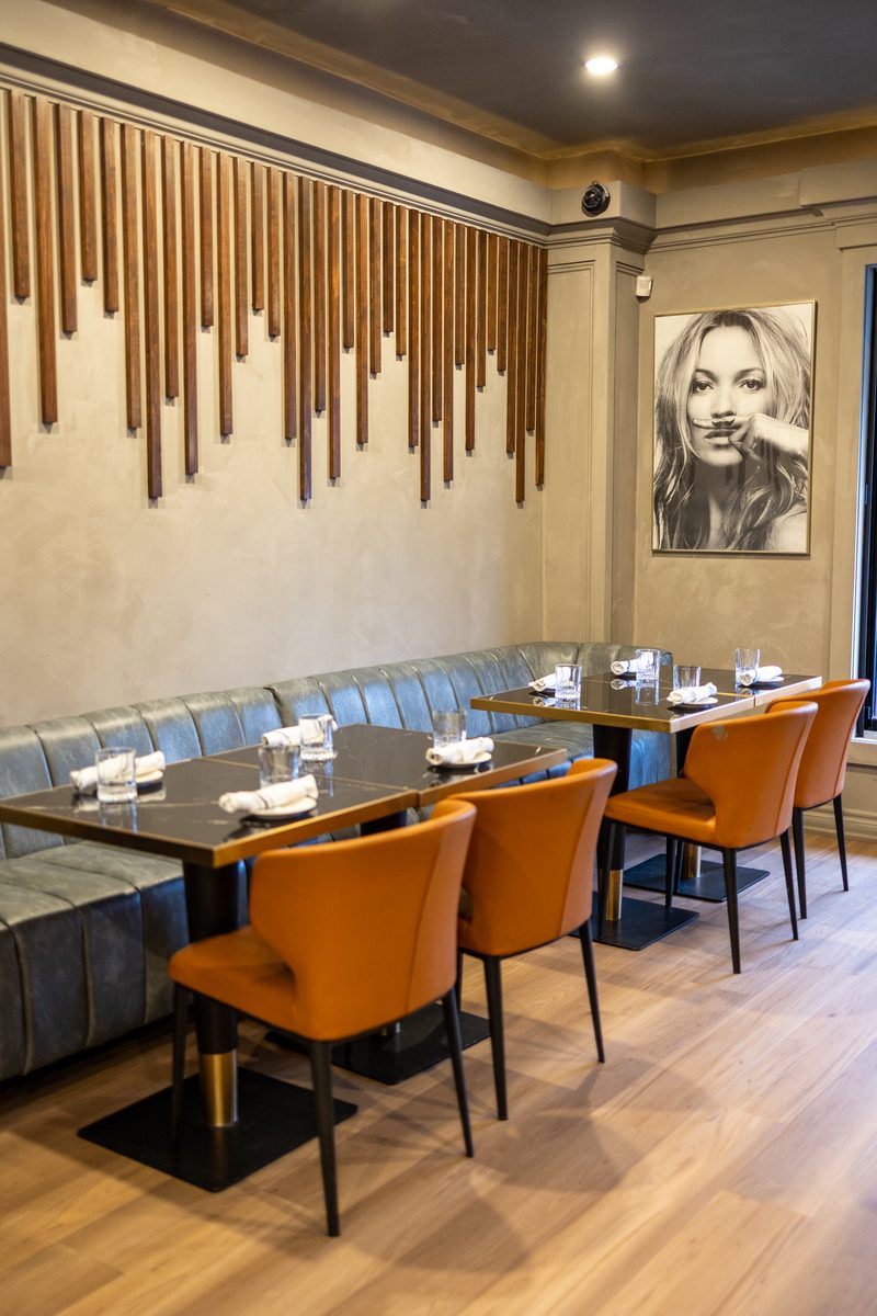 Green leather banquette seating beneath the sculptural wood-slat wall at Beacon Social House