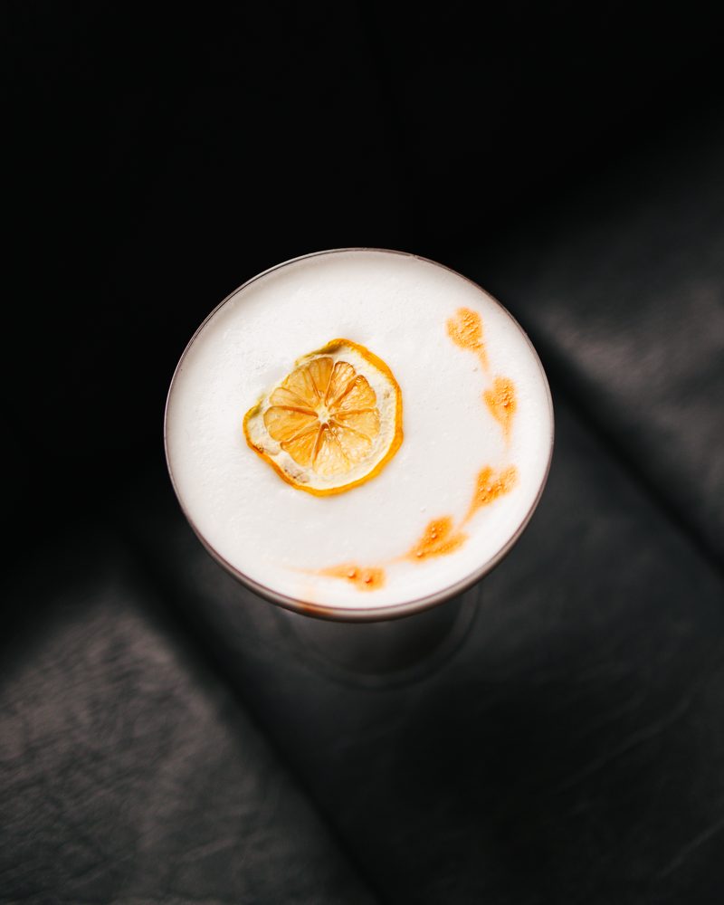 Overhead view of a foam-topped cocktail finished with a dried citrus wheel and orange bitters