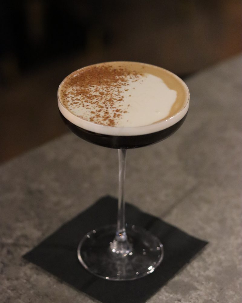An espresso martini in a coupe, dusted with cocoa, on the bar at Beacon Social House