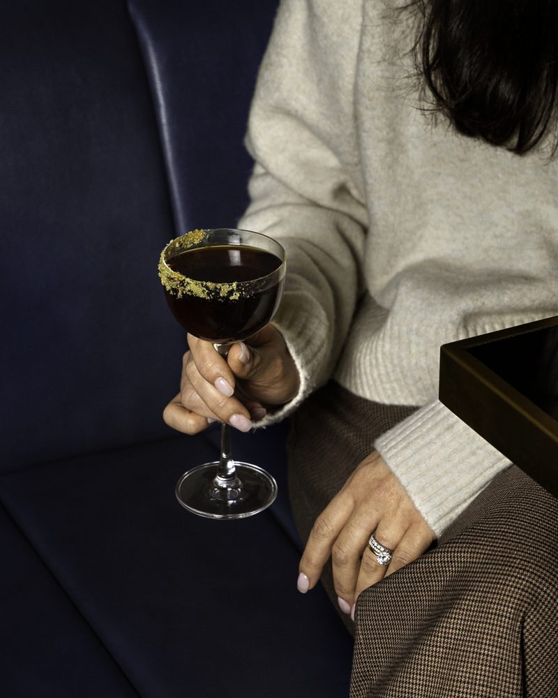 A gold-rimmed coupe cocktail held against the navy banquette at Beacon Social House