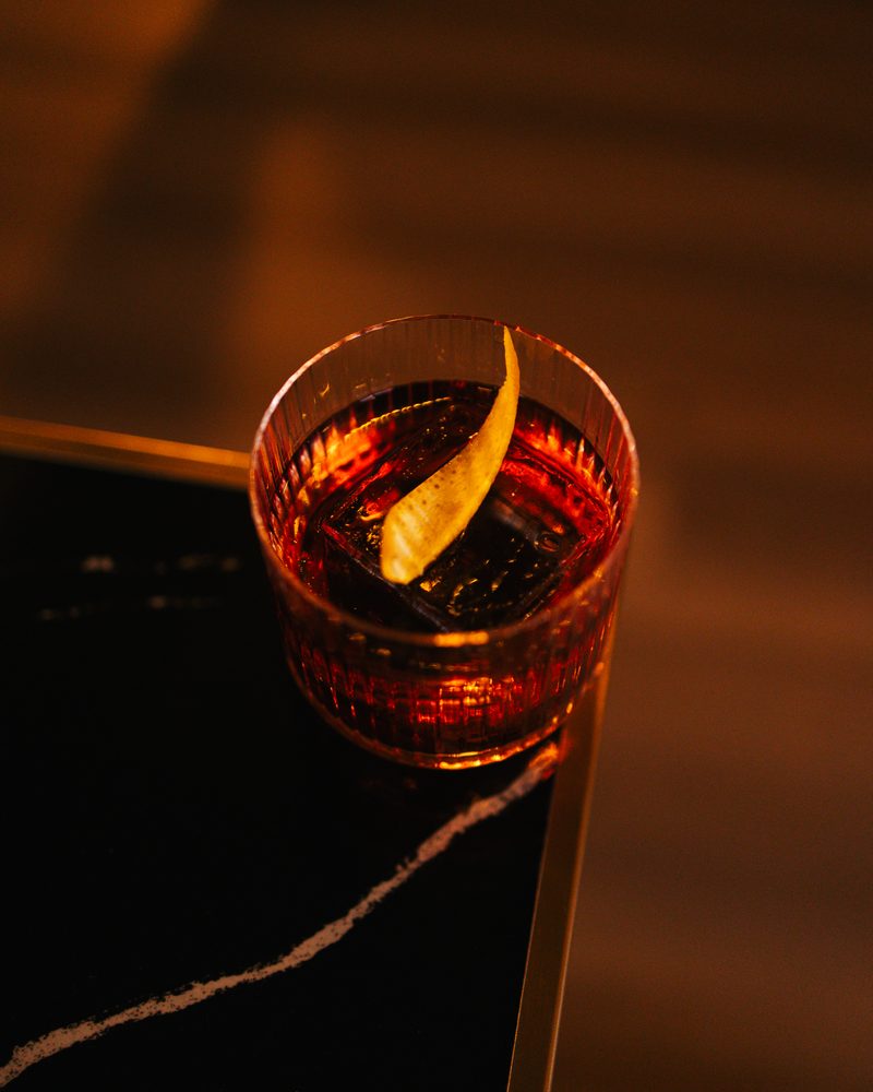 A Negroni over a large cube with an orange twist, on a black marble table at the Beacon bar