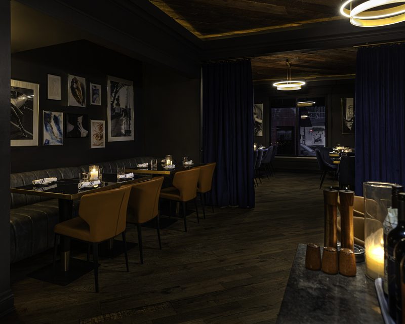 The Beacon dining room after dark — candlelight, navy velvet drapes and brass ring pendants