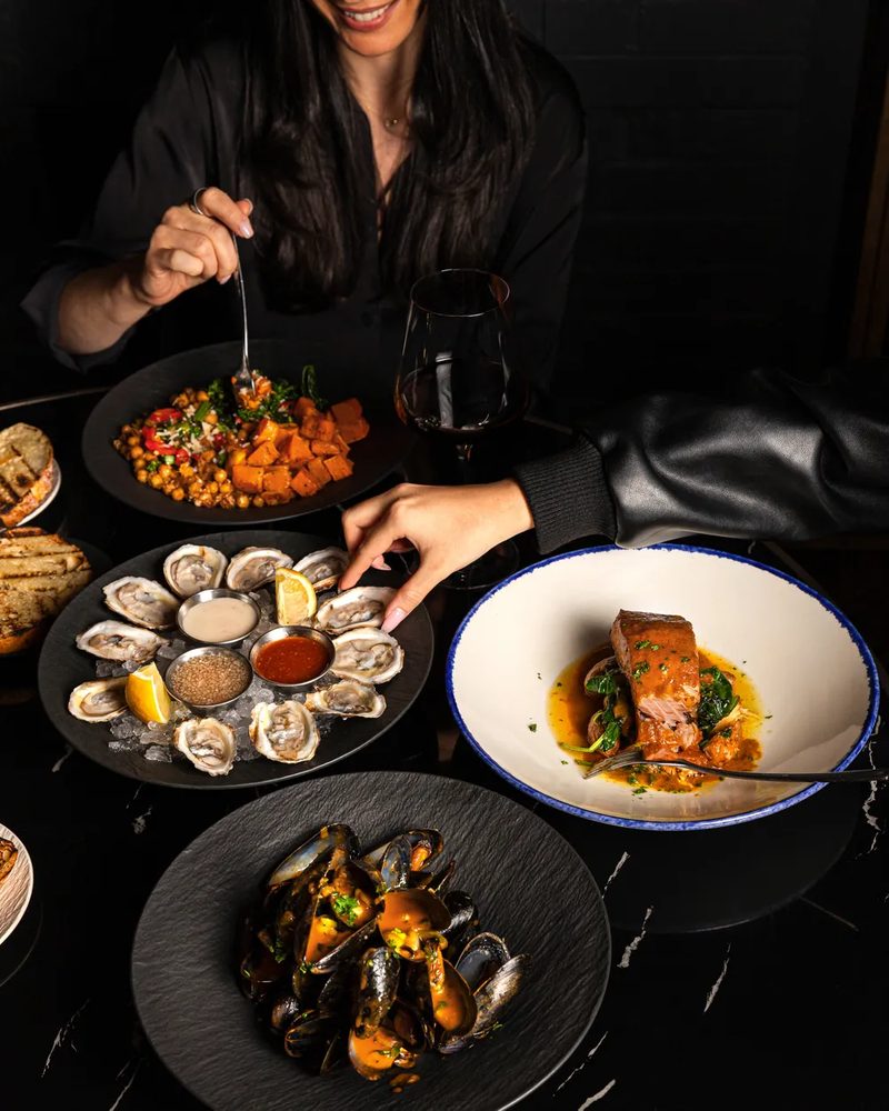 A shared table of oysters, mussels, salmon and roasted vegetables with red wine
