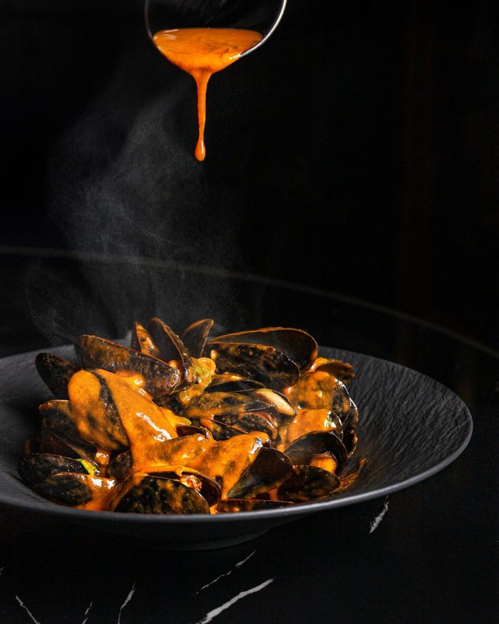 Steaming mussels in saffron tomato broth being finished tableside at Beacon Social House